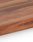 Close-up of a Le Creuset wooden cutting board showing the engraved brand name and rich wood grain texture.