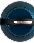 Top-down view of a Le Creuset enameled cast iron kettle in a deep teal blue color, featuring a black handle with a silver brand plate.