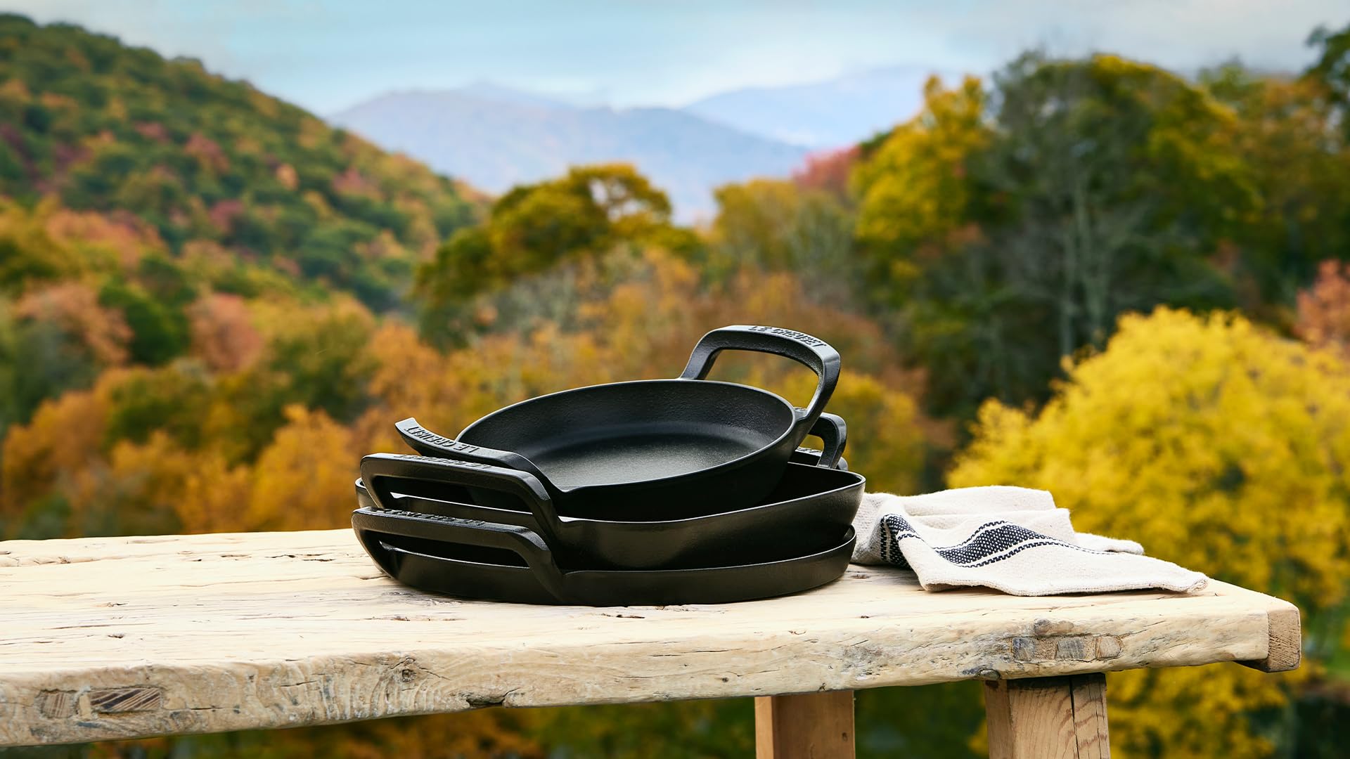 Black cast iron pans on a wooden table with a scenic background of mountains and trees.