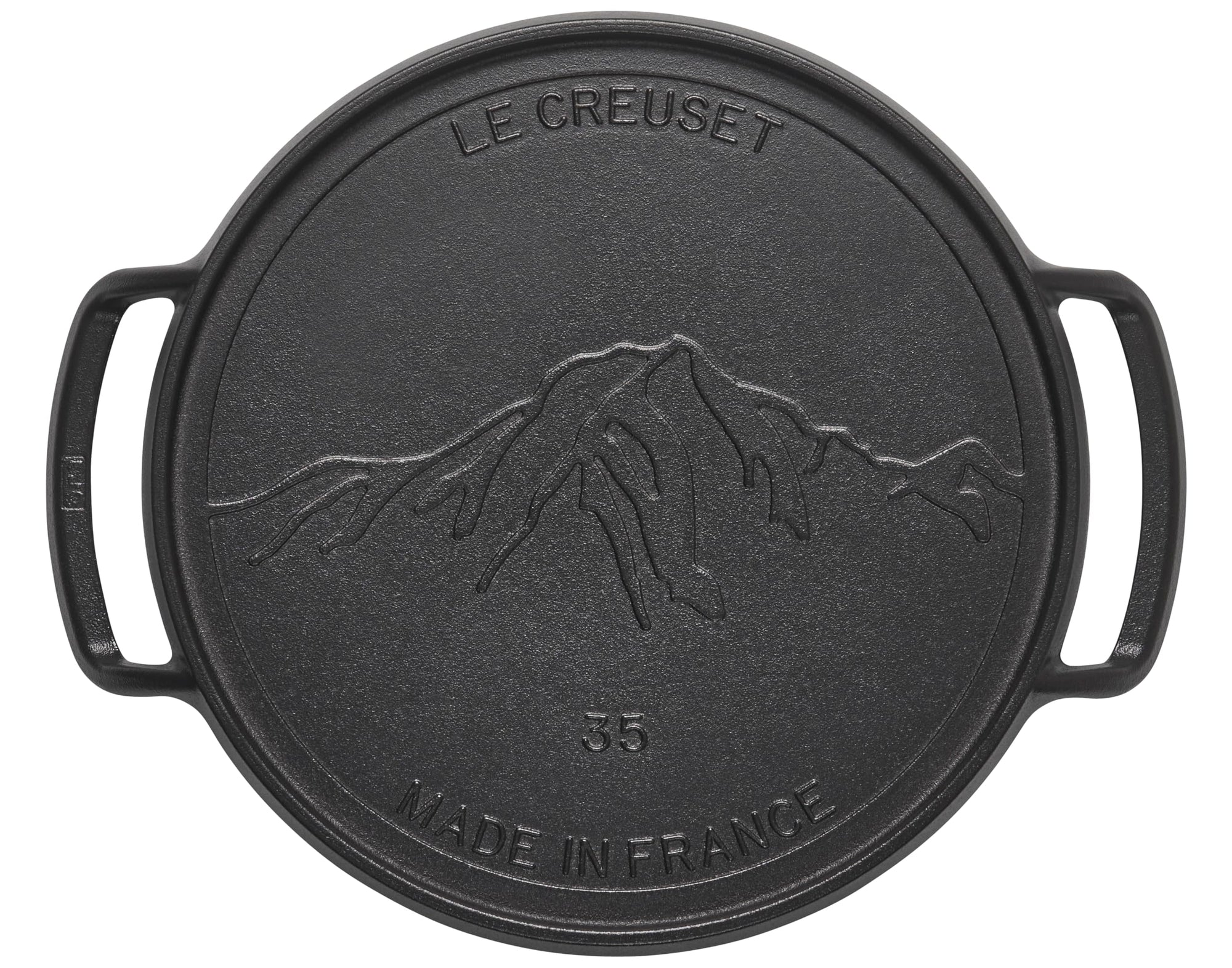 Black cast iron skillet with mountain design and 'Le Creuset' branding on a white background