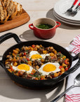 Breakfast dish with eggs and vegetables in a skillet on a wooden table.