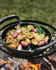 Black cast iron skillet with roasted vegetables over a campfire
