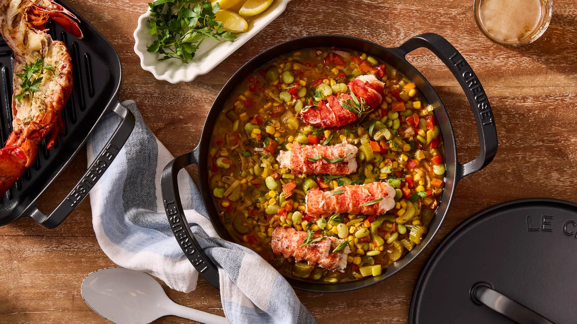 Lobster tail dish with vegetables in a cast iron skillet on a wooden table.