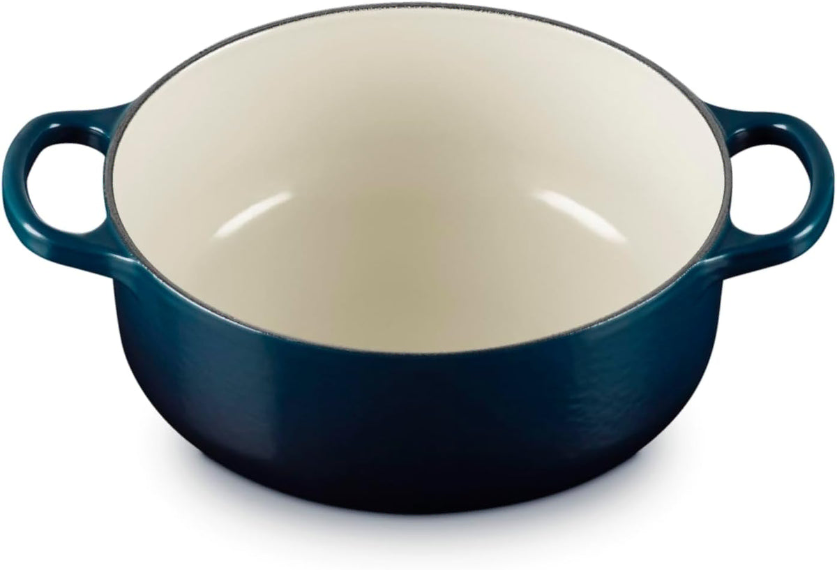 A navy blue enameled cast iron Dutch oven with a cream-colored interior and side handles, shown on a white background.