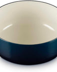 A navy blue enameled cast iron Dutch oven with a cream-colored interior and side handles, shown on a white background.