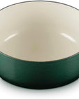 A dark green enameled cast iron Dutch oven with a cream-colored interior and side handles, shown on a white background.