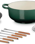 Le Creuset Dutch oven set on a white background, featuring a dark green enameled cast iron pot with a cream interior, a black burner stand, a silver lid, a small silver pot insert, and six metal skillets with wooden handles.