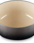 A round enameled cast iron Dutch oven with a dark gray exterior and a warm cream-colored interior, featuring two side handles.