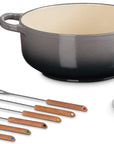 Le Creuset cast iron pot set with a dark gray to black ombre finish, cream interior, matching lid, and six copper utensils with wooden handles on a white background.