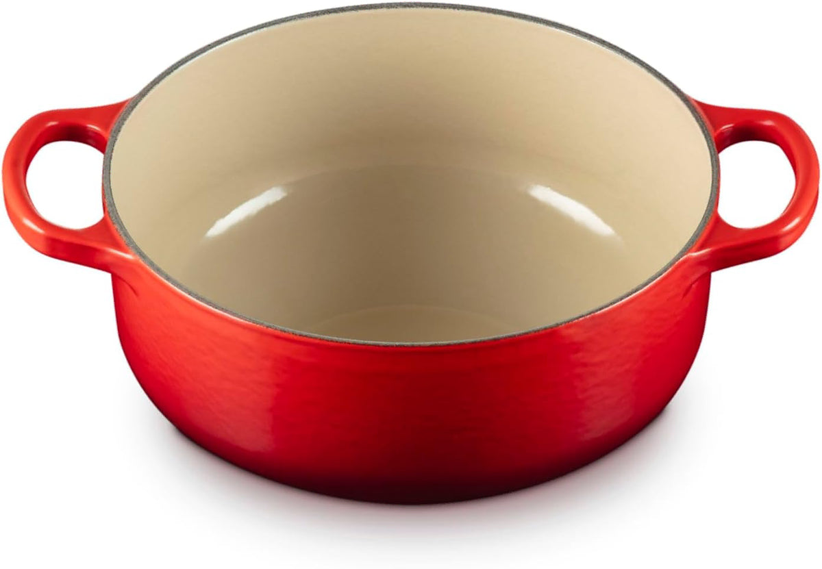 A red enameled cast iron Dutch oven with a cream-colored interior and side handles, shown from a high angle on a white background.