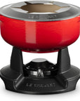 A red Le Creuset enameled cast iron pot with a matching red lid, shown on a black Le Creuset burner base against a white background.