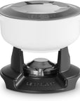 A Le Creuset white enameled cast iron pot with a dark gray lid, shown on a black Le Creuset burner base against a white background.