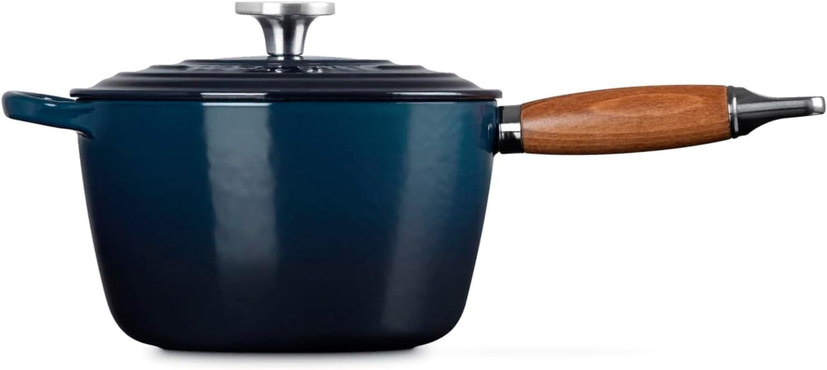 Side view of a dark blue enameled cast iron saucepan with a wooden handle and a matching lid, shown on a plain white background.