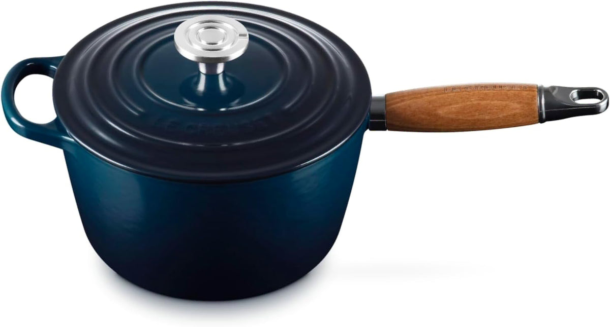 A dark blue enameled cast iron saucepan with a matching lid and a brown wooden handle, shown on a white background.