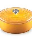 A Le Creuset round enameled cast iron Dutch oven with lid, in a vibrant orange-yellow color, featuring side handles and a silver knob, set against a plain white background.