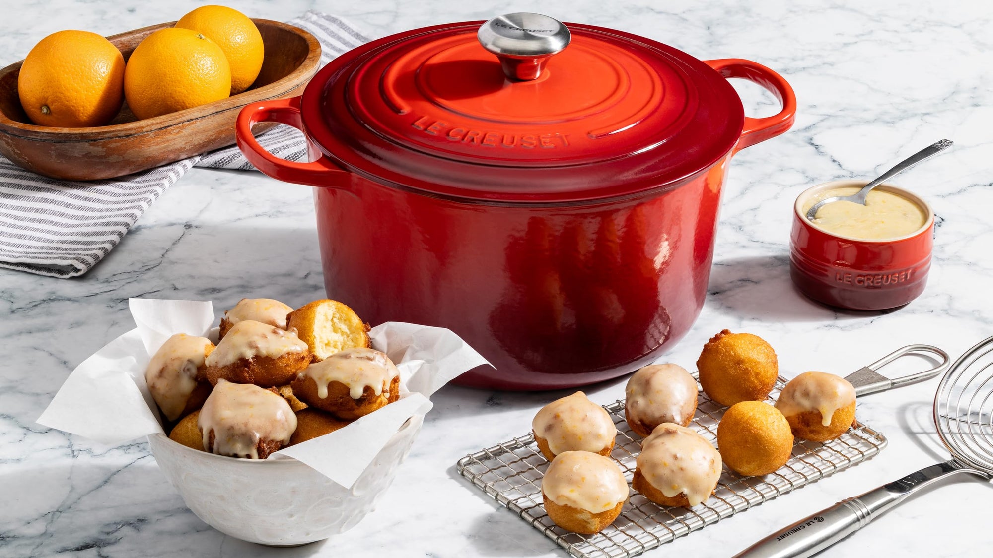 Red cast iron Dutch oven on a marble surface with baked goods and oranges.