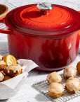 Red cast iron Dutch oven on a marble surface with baked goods and oranges.