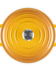 A top-down view of a Le Creuset round enameled cast iron pot with a matching lid, in a vibrant yellow color, set against a solid white background.