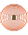 A top-down view of a Le Creuset round Dutch oven lid in a metallic rose gold finish, featuring concentric circular ridges and a gold-toned central knob on a white background.
