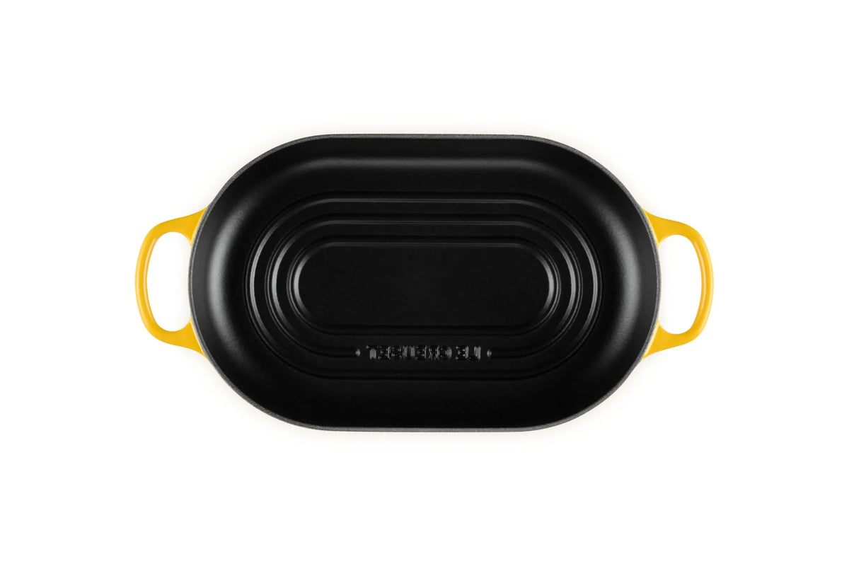 A black oval cast iron skillet with bright yellow handles, shown from a top-down view on a solid white background.