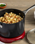 Le Creuset Essential Non-stick Ceramic 3 qt Saucepan with Lid with cooked mac and cheese next to bowls and forks on a wooden surface