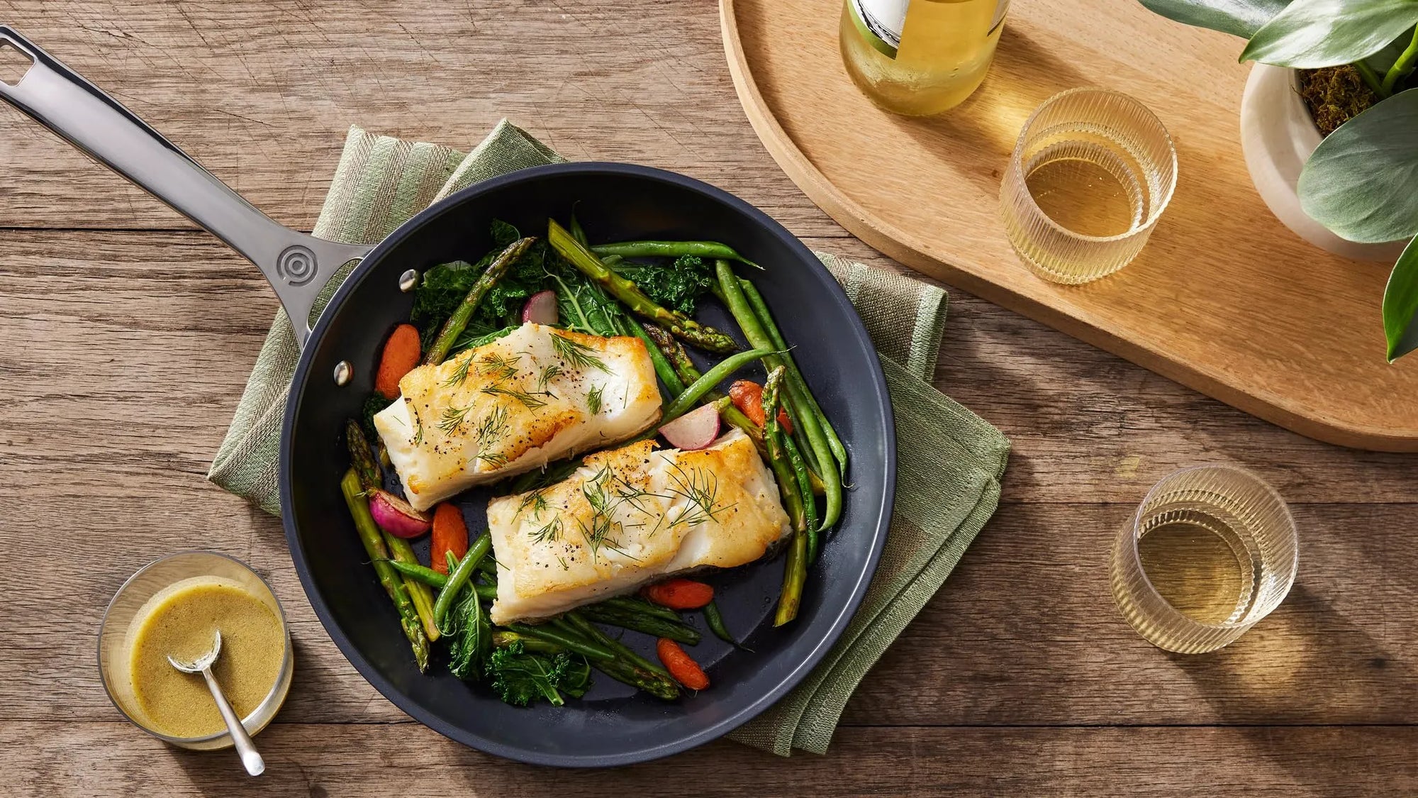 Top view of Le Creuset Essential Non-stick Ceramic 8" Fry Pan with cooked fish and vegetables next to drinks and a sauce on a wooden surface