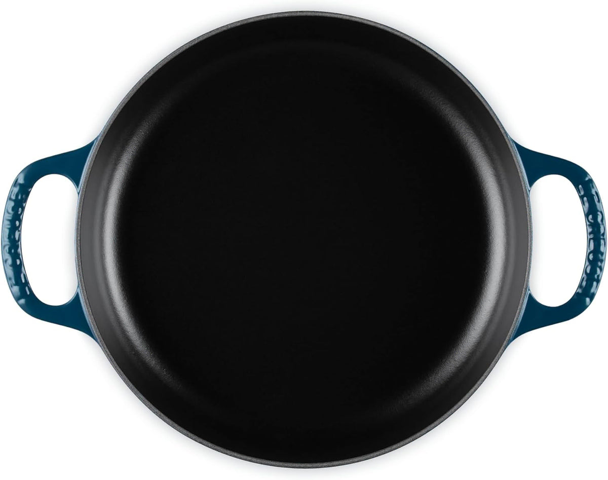 A top-down view of a round cast iron skillet with a black interior and a dark teal blue exterior handles, shown on a solid white background.