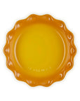A small scalloped ceramic plate in a vibrant yellow-orange color, photographed from directly above on a clean white background.
