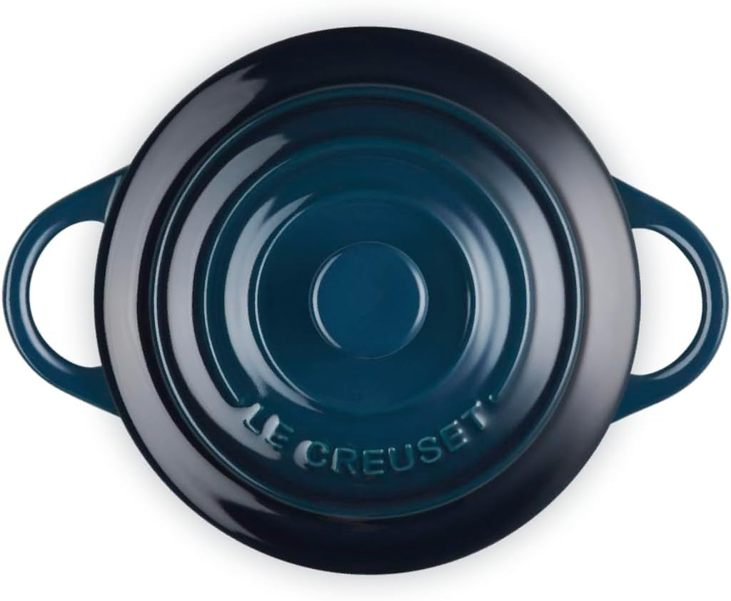 Top-down view of a Le Creuset round lidded casserole dish in a dark teal enamel finish, featuring two side handles and the embossed Le Creuset brand name on the bottom of the lid.