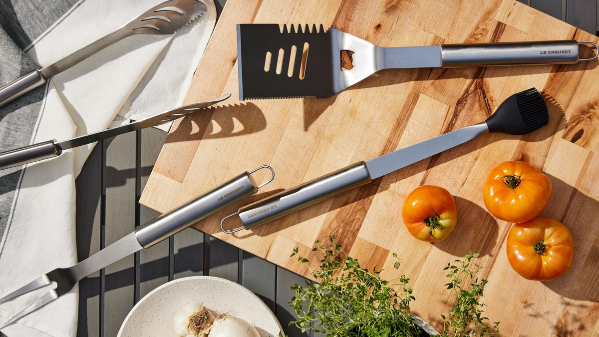 Grilling tools and vegetables on a wooden cutting board