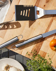 Grilling tools and vegetables on a wooden cutting board