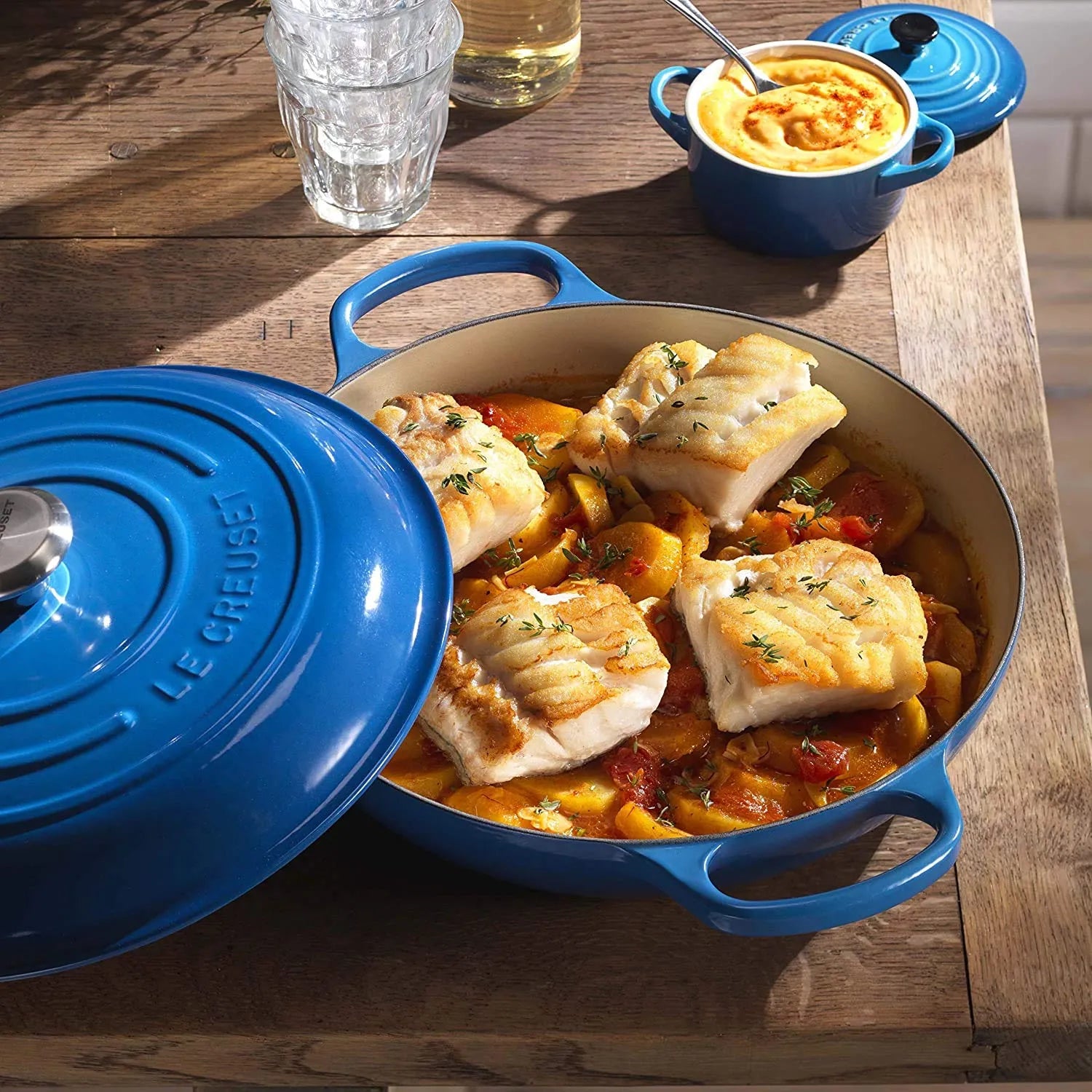 Blue Le Creuset casserole dish with fish and vegetables on a wooden table