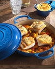 Blue Le Creuset casserole dish with fish and vegetables on a wooden table