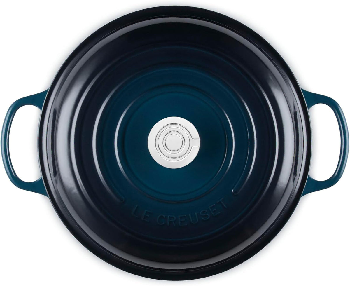 Top-down view of a Le Creuset round enameled cast iron pot or Dutch oven with side handles, showing a dark navy blue interior and a silver metal center insert.