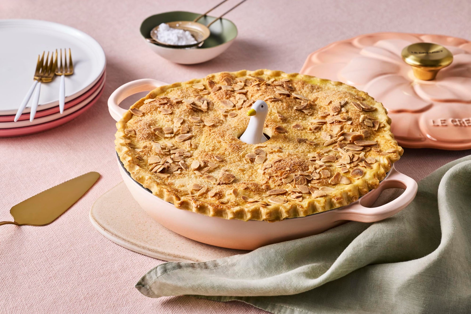 Pie in a ceramic dish on a table with plates and utensils.