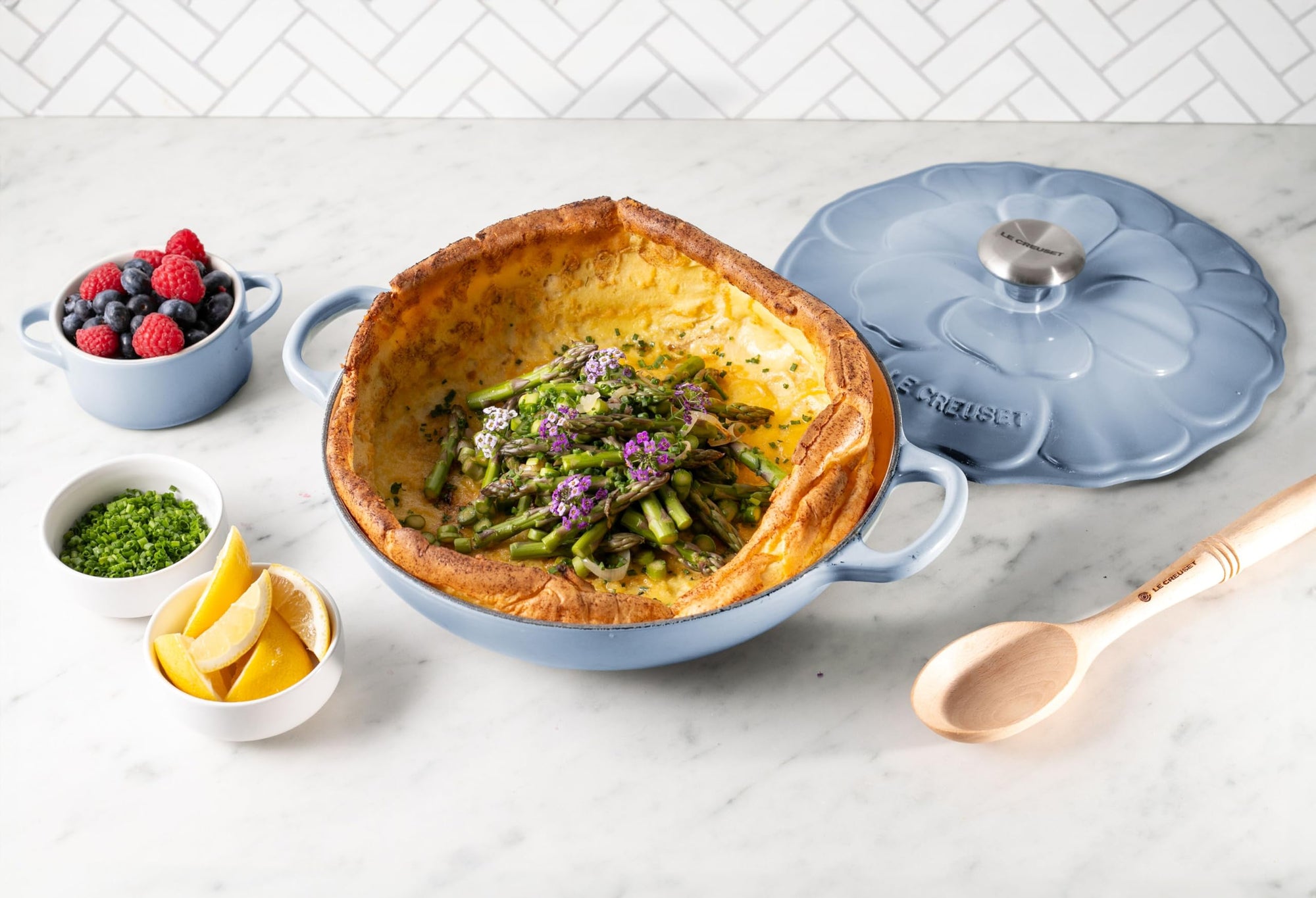 Dish with green vegetable dish on a marble countertop with a blue lid and small bowls of ingredients.