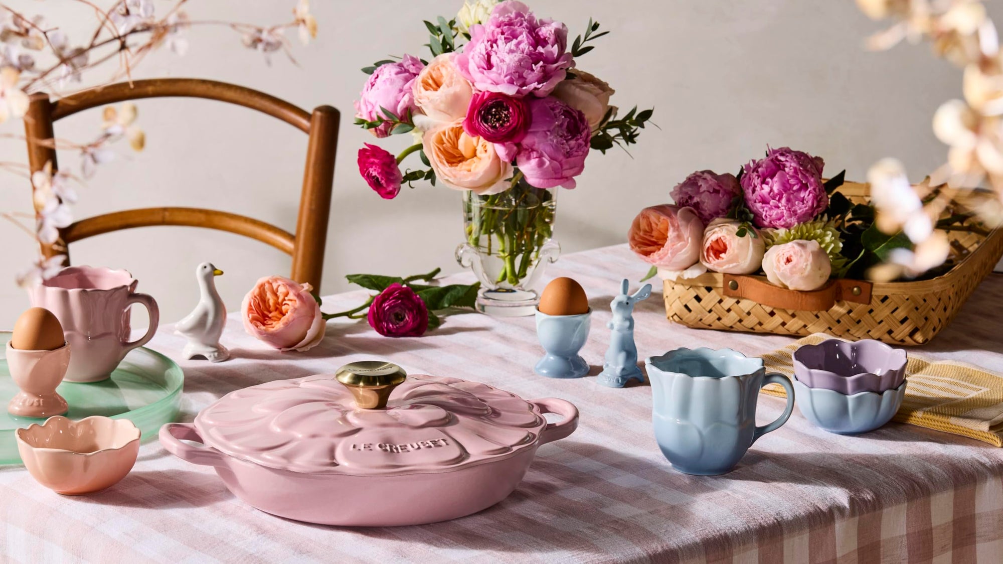 Pastel-colored tableware on a checkered tablecloth with flowers and eggs.