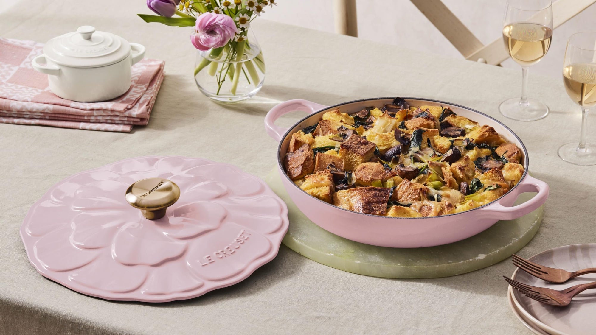 Pink ceramic dish with food on a table with flowers and wine glasses
