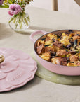 Pink ceramic dish with food on a table with flowers and wine glasses