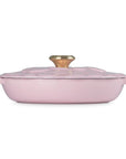 Pink casserole dish with gold knob on a white background
