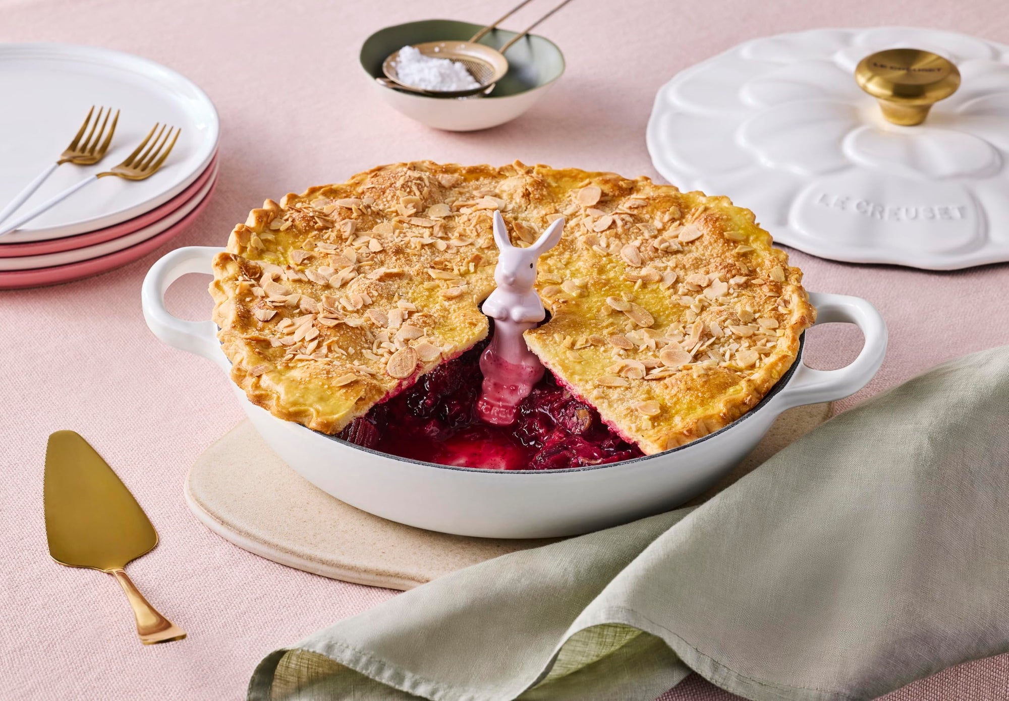Pie with a slice cut out, placed in a white dish on a table with a green napkin and gold utensils.