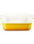 A rectangular ceramic baking dish with a yellow exterior and a white interior, featuring small side handles on a clean white background.