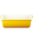 A rectangular ceramic baking dish with a bright yellow exterior and a white interior, featuring small side handles, shown on a plain white background.