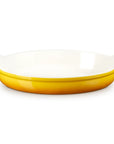 An oval ceramic baking dish with a glossy white interior and a vibrant yellow exterior, featuring small side handles on a clean white background.