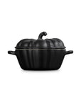 Side view of a black cast-iron pumpkin-shaped lidded cocotte with side handles, shown on a plain white background.