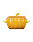A yellow-orange pumpkin-shaped ceramic casserole dish with a matching lid and small side handles, centered on a plain white background.