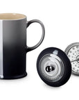 A ceramic French press pitcher with a black-to-gray gradient finish, shown alongside its black lid and metal infuser filter on a white background.