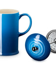 A vibrant blue coffee French press with a cream-colored interior, shown alongside its black lid and a silver metal infuser filter on a clean white background.