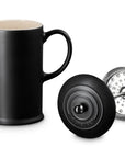 A matte black coffee french press with a cream-colored interior, shown alongside its black lid and a silver metal infuser filter on a clean white background.