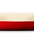 A rectangular ceramic baking dish with a glossy red exterior and a cream-colored interior, featuring integrated side handles, shown on a plain white background.